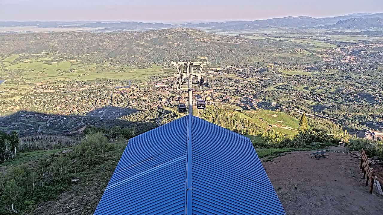 A chairlift ascends a mountain on a clear day, overlooking a sprawling town nestled in a valley below.