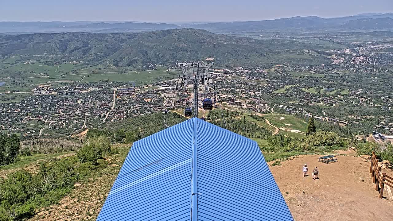 A chairlift ascends a mountain on a clear day, overlooking a sprawling town nestled in a valley below.