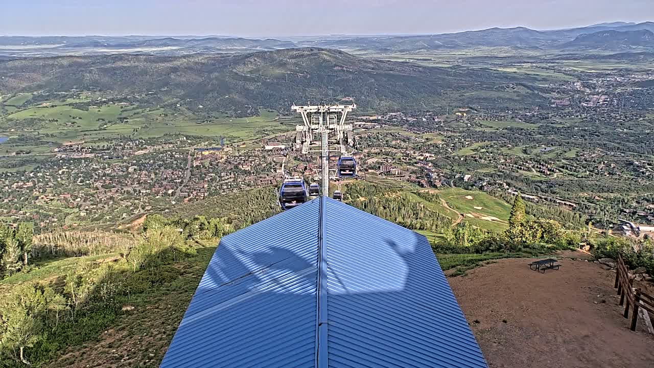 A chairlift ascends a mountain overlooking a valley town on a clear, sunny day.