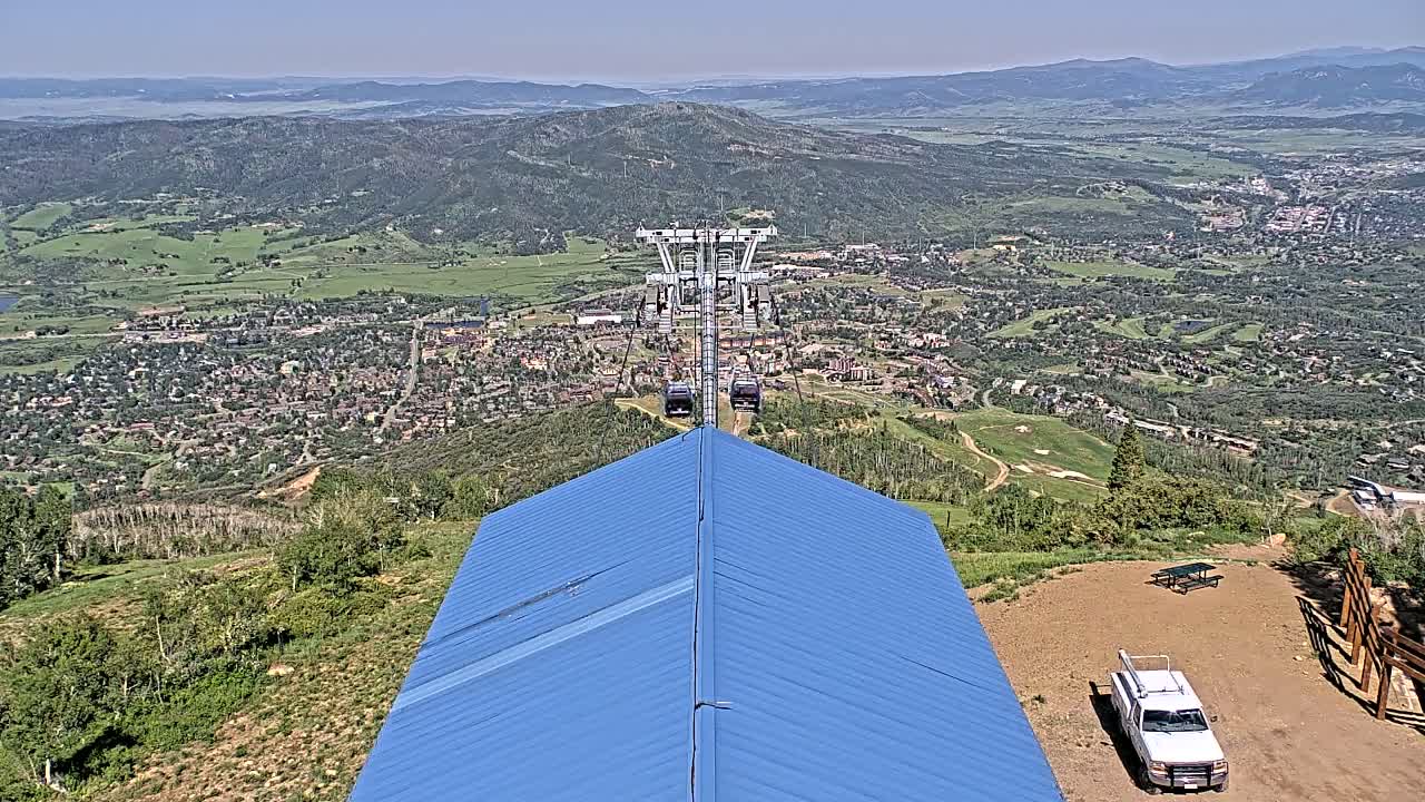A chairlift ascends a mountain on a clear, sunny day, overlooking a sprawling town nestled in a valley below.
