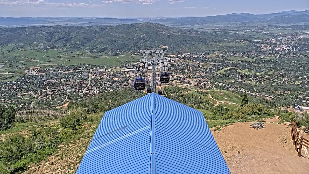 A chairlift ascends a mountain overlooking a valley town on a sunny day.