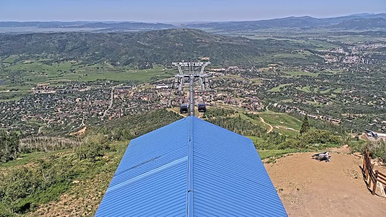 A blue roofed structure overlooks a valley town with a chairlift in the distance on a sunny day.