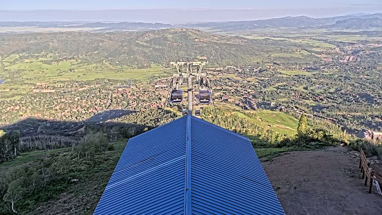 A chairlift ascends above a mountain town nestled in a valley, under a clear sky.