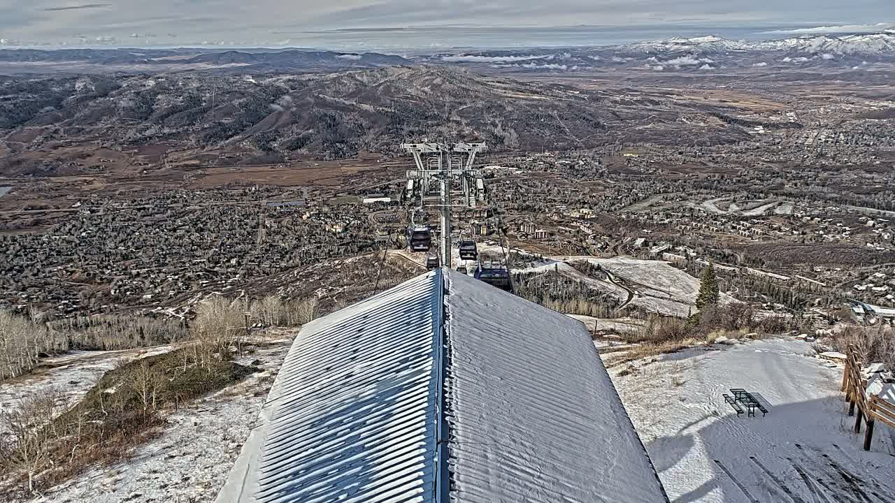 A nighttime view from a hilltop shows a brightly lit town below, a ski lift, and a two-toned roof in the foreground.