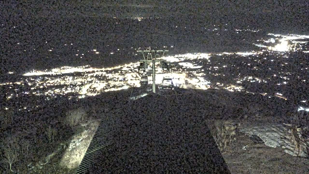 A cable car system ascends a dark mountainside at night, offering a panoramic view of a brightly lit city spread out below under clear skies.