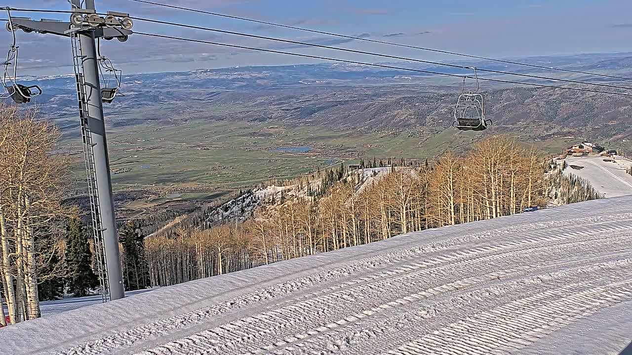 A snowy ski slope with a chairlift and a view of a valley under a clear sky.