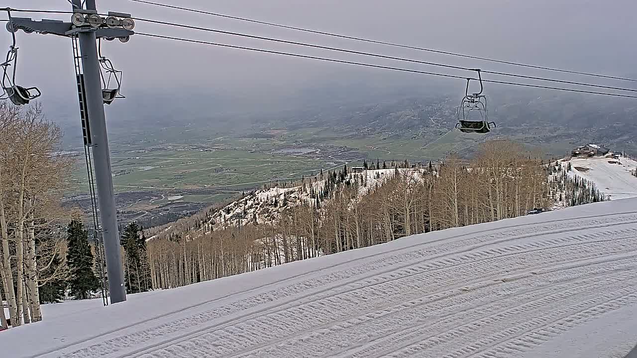 A snowy ski slope with a chairlift and a view of a valley under an overcast sky.