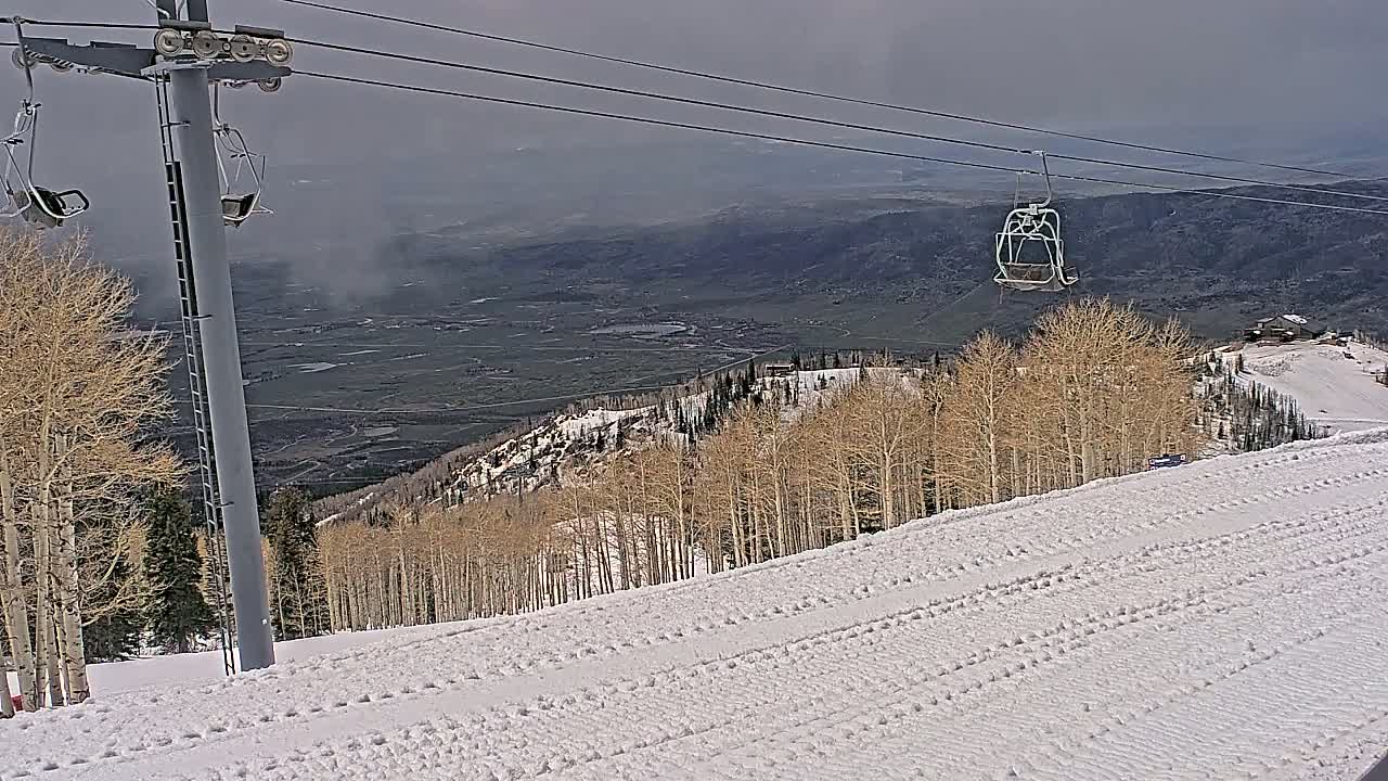 A snowy ski slope with a chairlift and bare aspen trees overlooks a hazy valley.