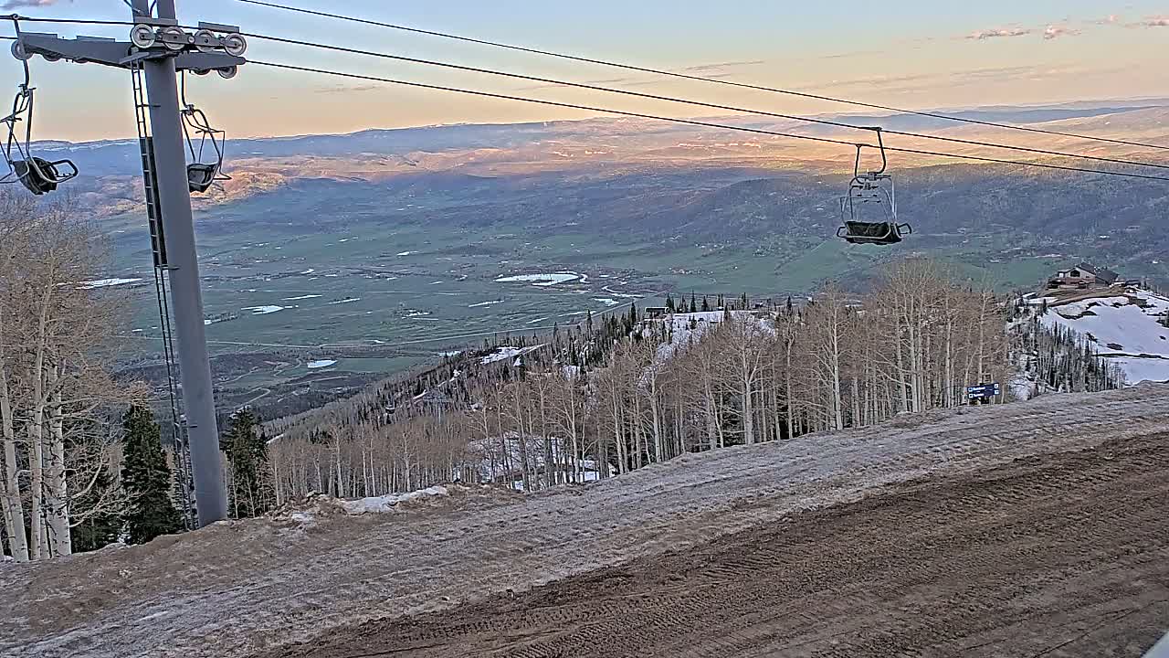 A chairlift ascends a snowy mountain slope overlooking a vast valley under a clear, twilight sky.