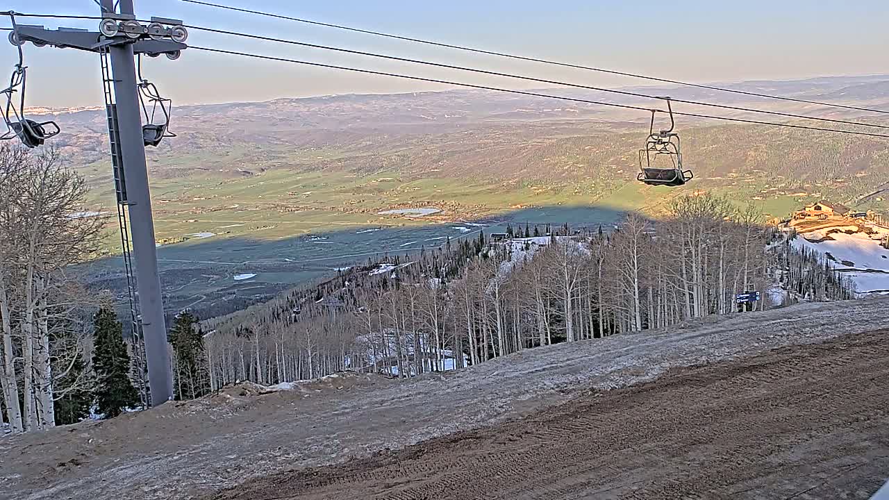 A chairlift ascends a mountainside overlooking a vast valley under a clear, bright sky.