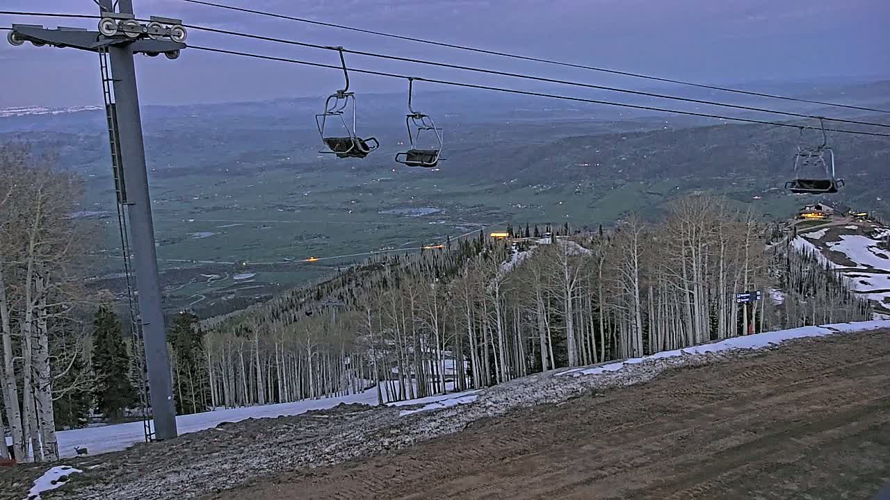 Empty chairlifts hang over a snow-dusted mountain slope overlooking a valley at dusk.