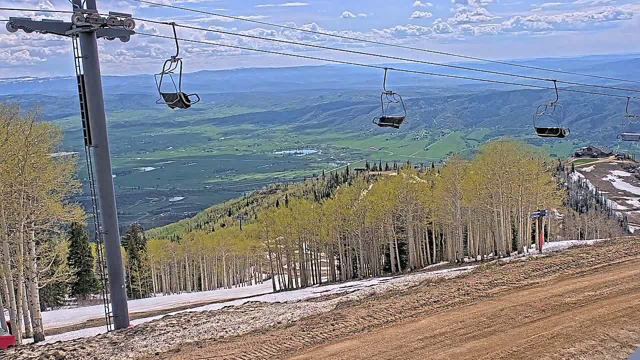 A mostly clear sky overlooks a mountain ski lift with several empty chairs, a sparsely populated aspen grove, and a valley below.
