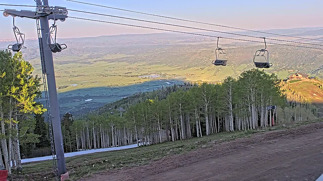 A chairlift ascends a mountainside overlooking a vast valley under a clear, sunset sky.