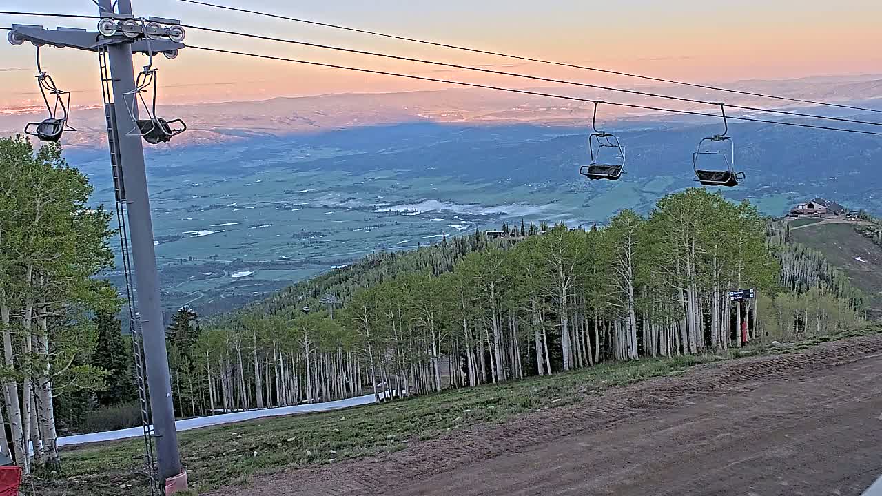 A ski lift with empty chairs overlooks a valley at sunset, with a forest of aspen trees in the foreground.