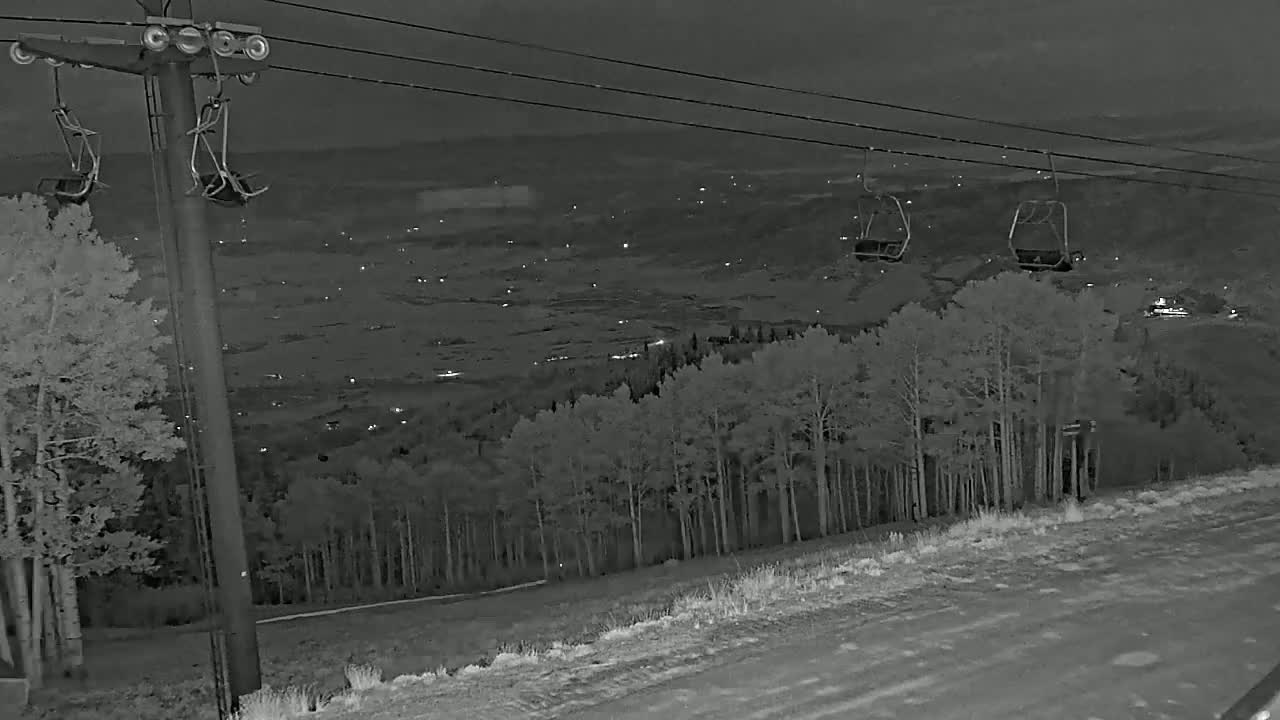 A nighttime, snow-covered ski lift overlooks a valley with distant lights under a dark sky.