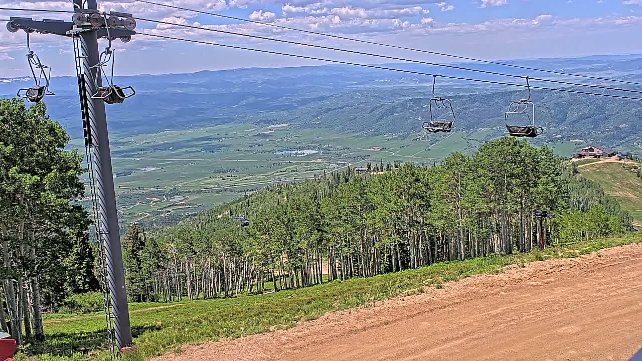 A sunny day reveals a mountain vista with a chairlift and empty chairs overlooking a valley and dense forest.