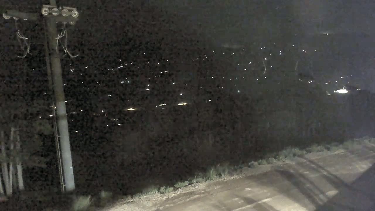 A nighttime view shows a dirt road, a utility pole, and a distant collection of faint lights in the dark.