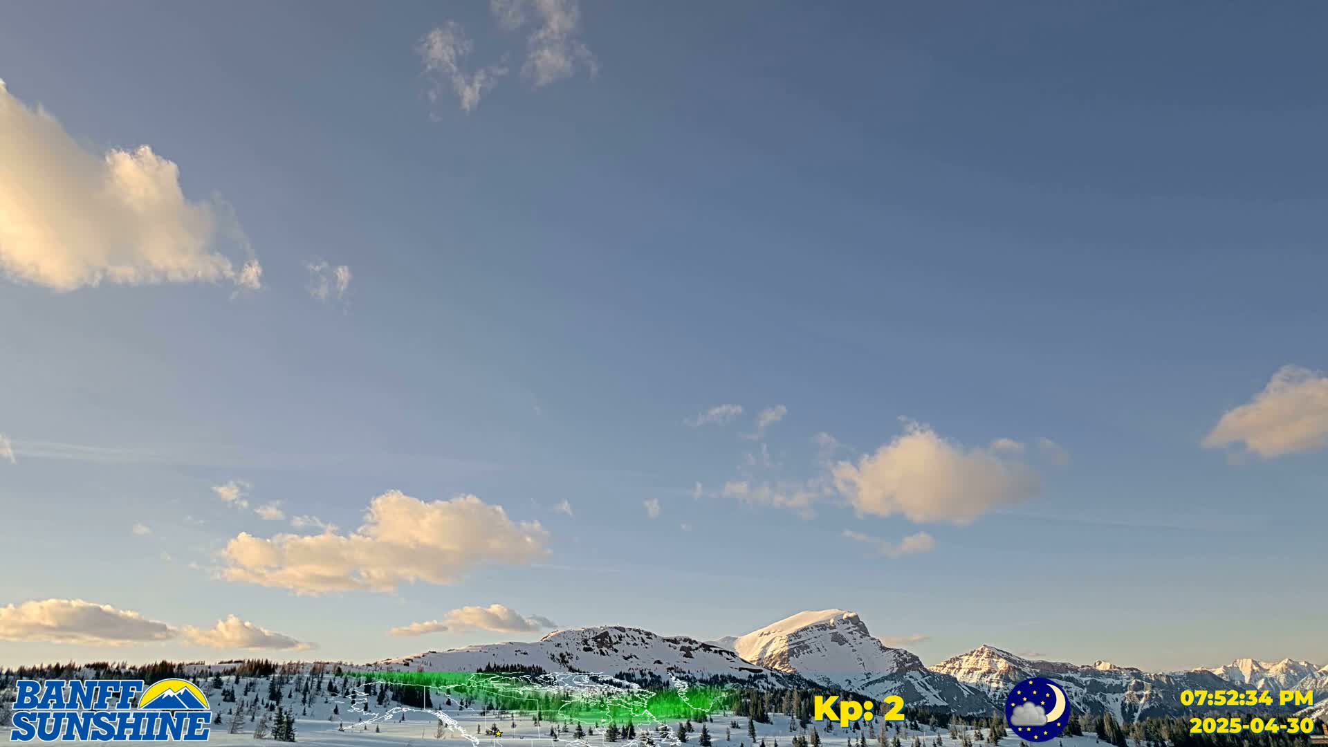 A partly cloudy, late afternoon sky overlooks snow-covered mountains.