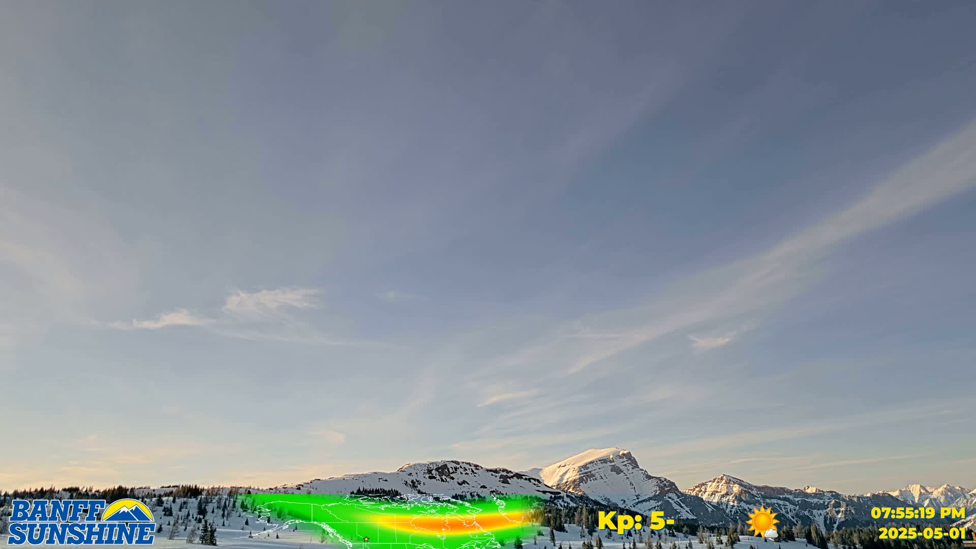 A mostly clear, light blue sky with wispy clouds over snow-covered mountains.