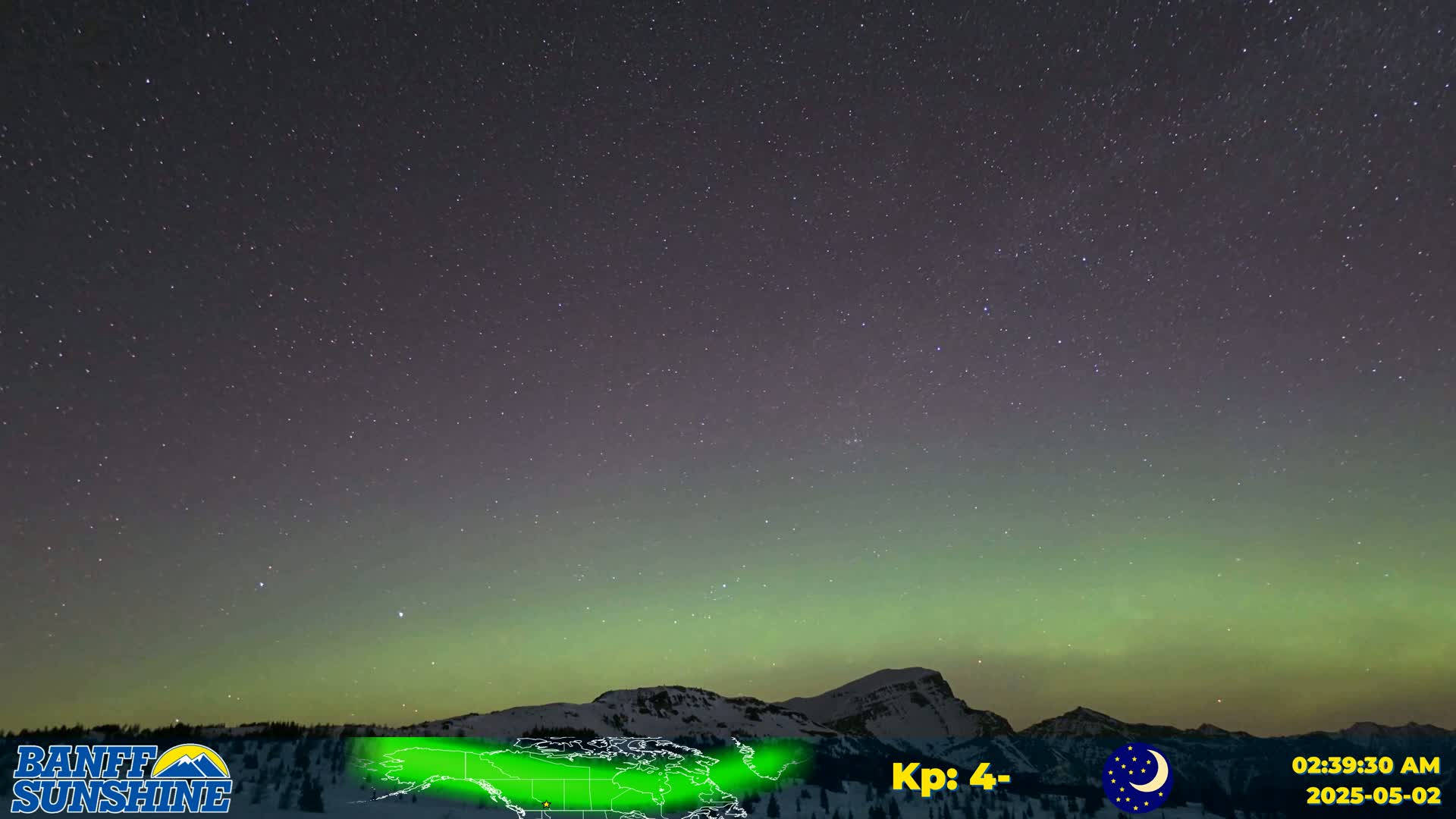 A vibrant green aurora borealis illuminates a night sky full of stars above a snow-covered mountain range.