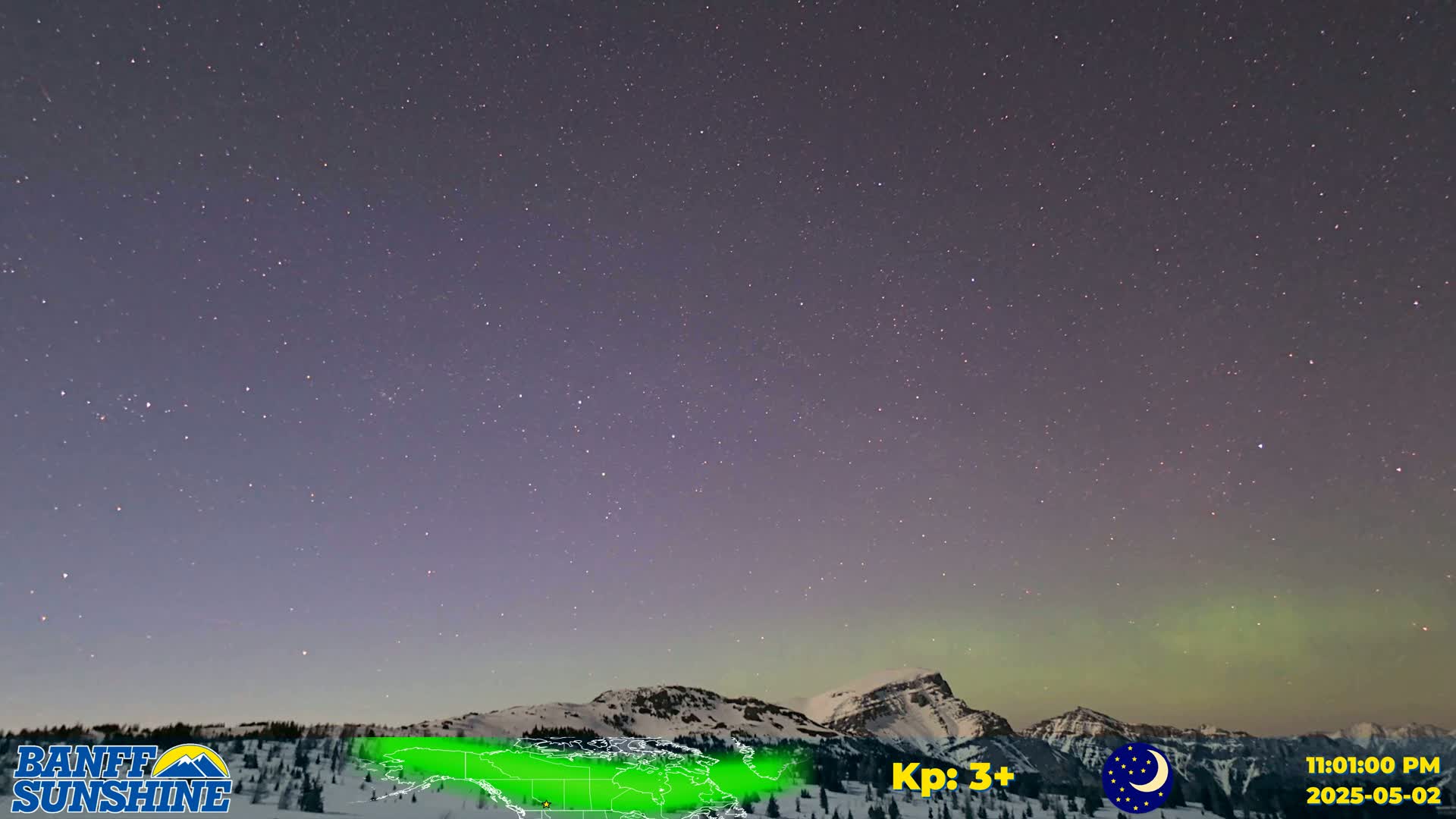 A night sky filled with stars and a faint aurora borealis displays over snow-covered mountains.