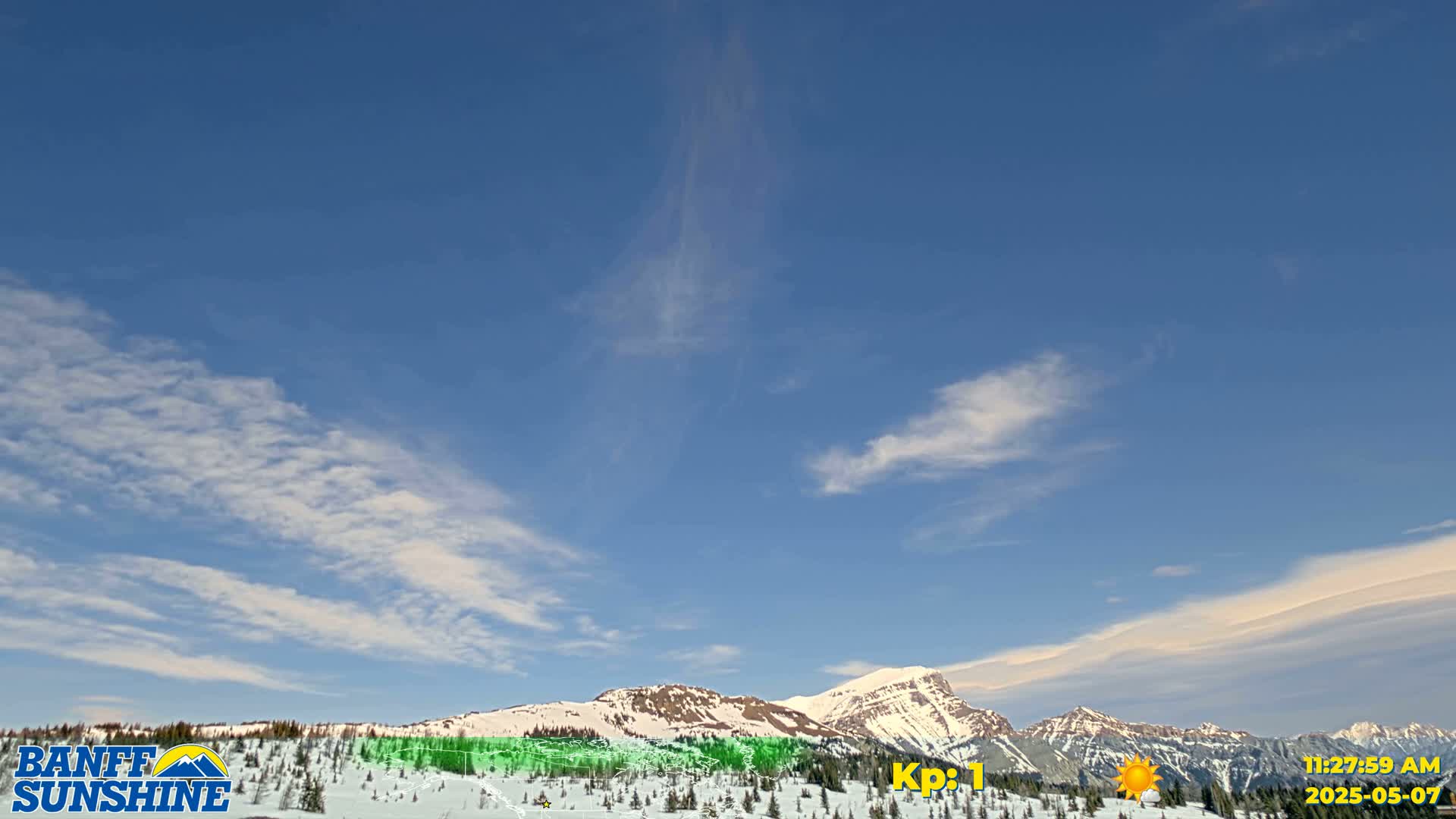 A mostly clear blue sky with wispy clouds over snow-covered mountains.