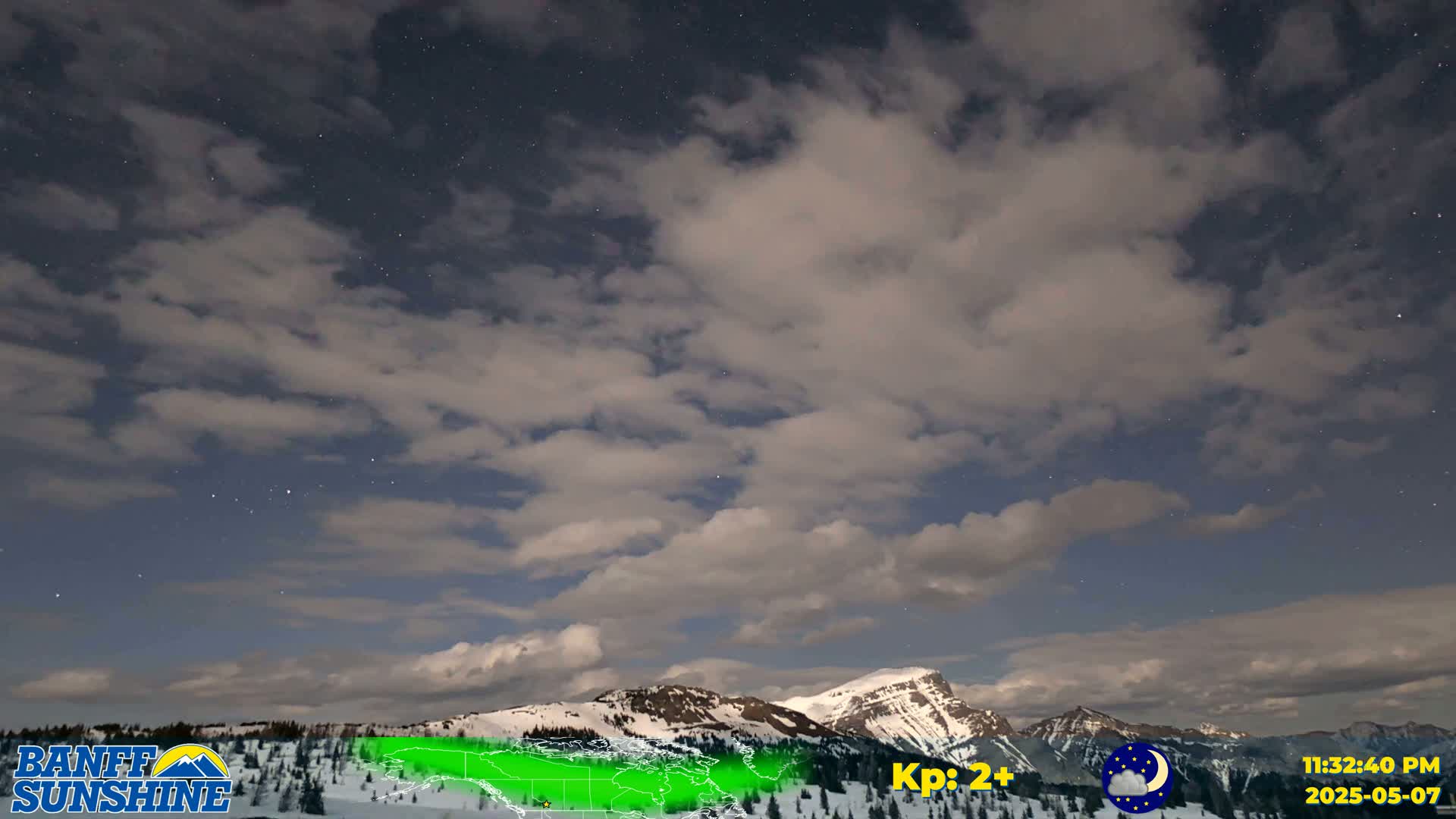 A partly cloudy night sky over snow-covered mountains.