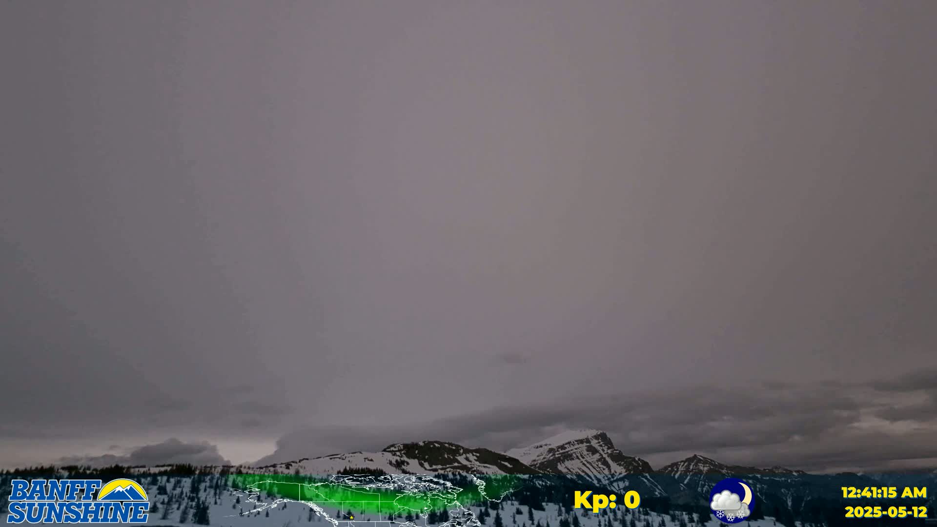 Overcast, dark gray skies hang over snow-covered mountains and a coniferous forest.