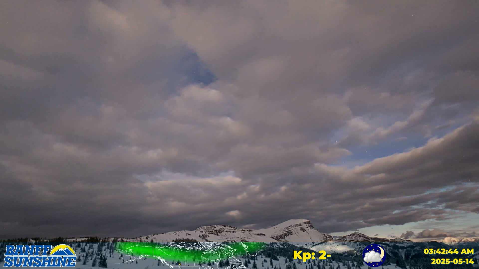 A mostly cloudy, pre-dawn sky hangs over snow-covered mountains.