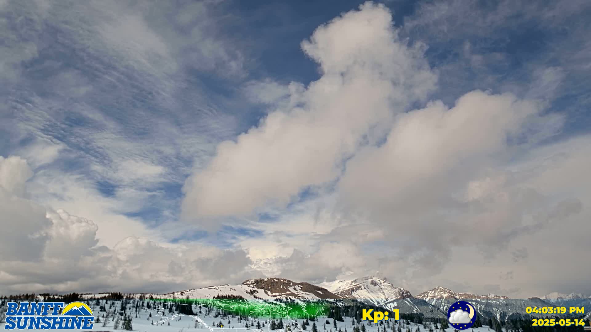A partly cloudy sky with puffy white clouds over snow-covered mountains.