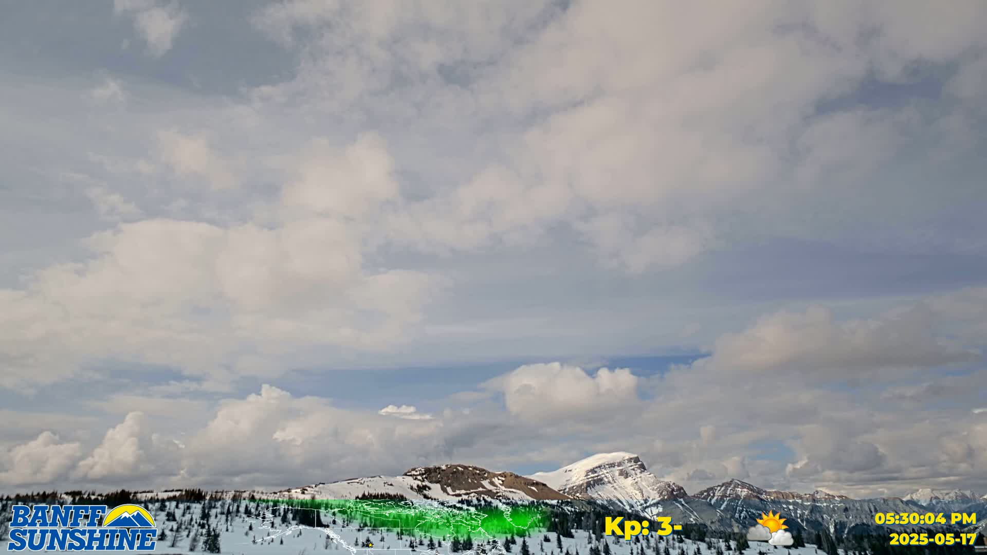 A partly cloudy sky overlooks snow-covered mountains.