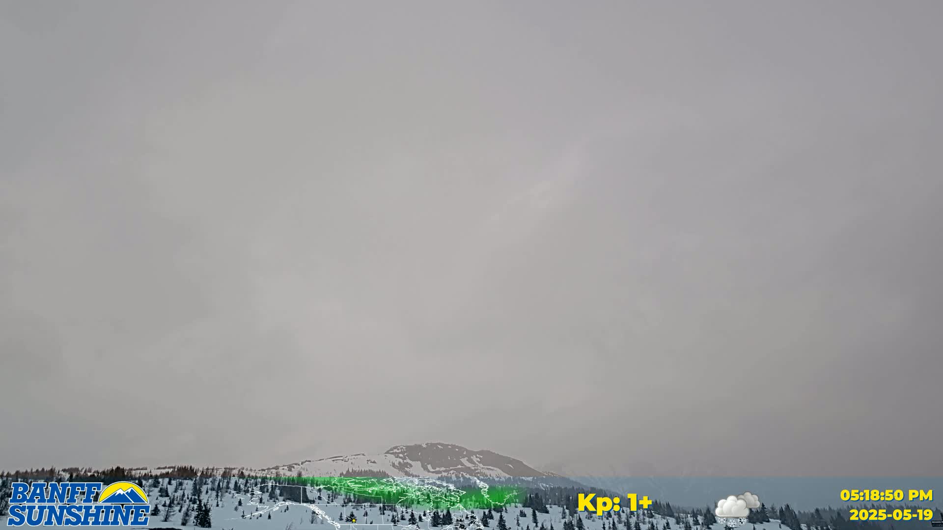 A hazy, overcast sky hangs over a snow-covered mountain range and a coniferous forest.