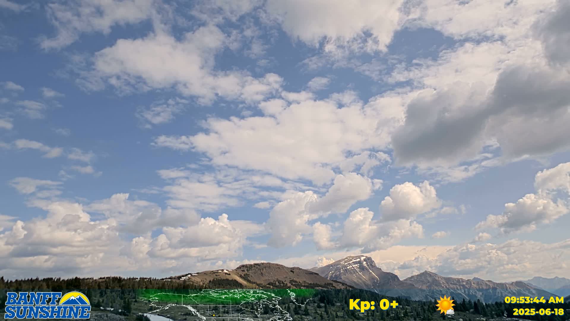 A partly cloudy sky over a mountain range with some patches of snow on the peaks.