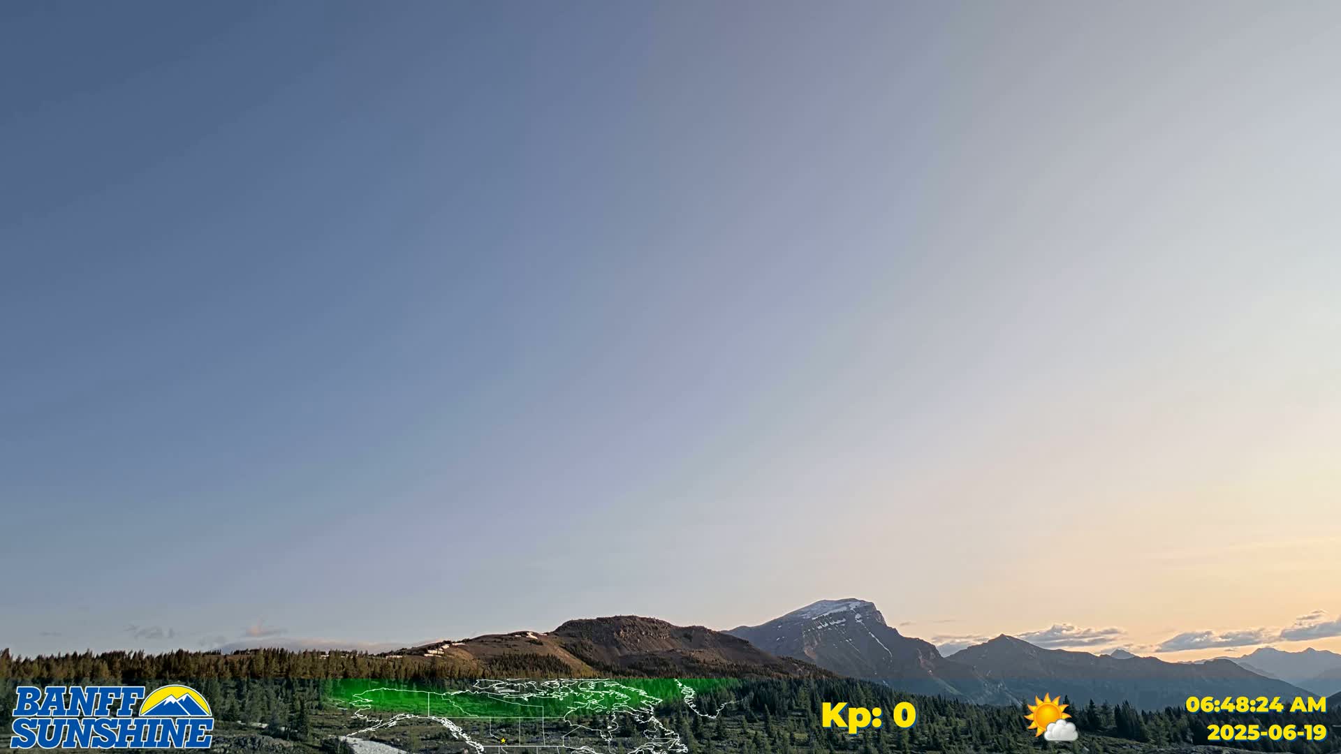 A mostly clear sky over a mountain range with some trees and a small amount of snow visible on the peaks.