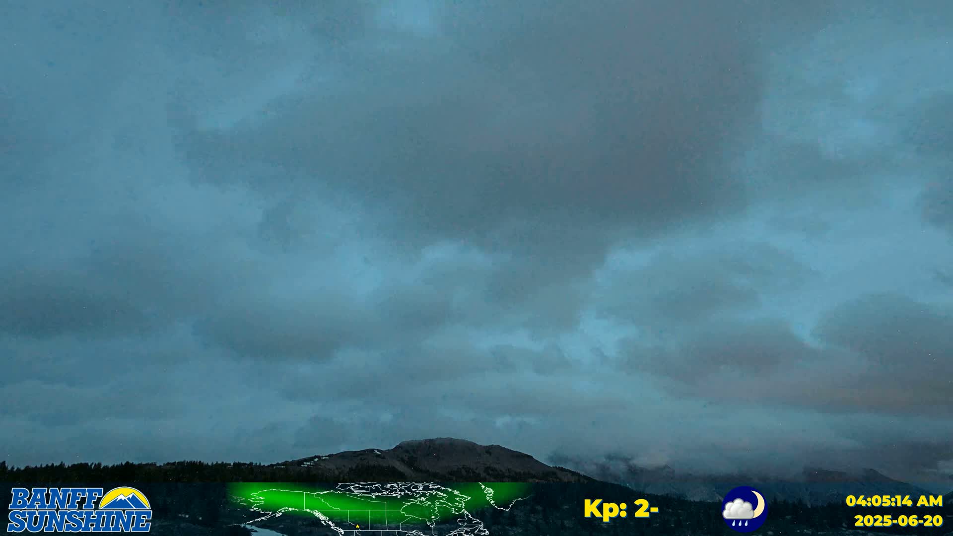 A dark, overcast sky hangs over a mountain range under conditions of light rain.