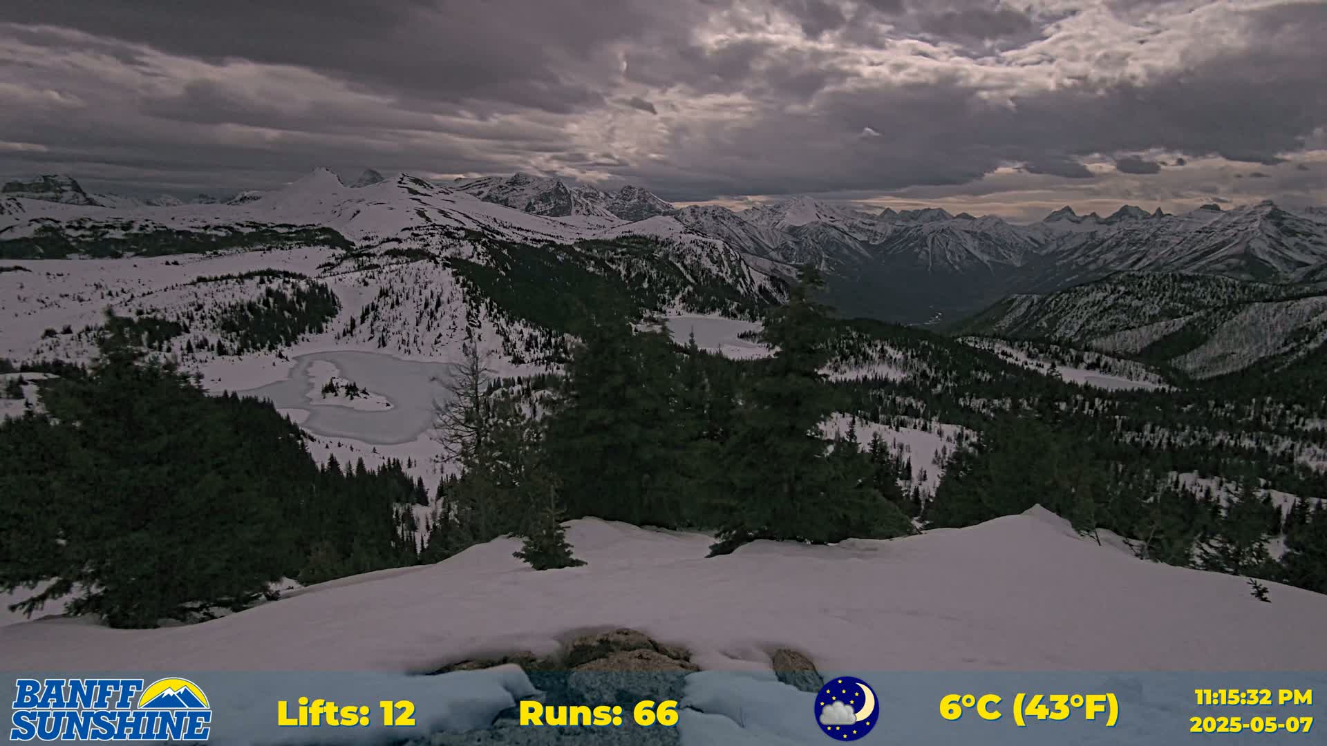 A snow-covered mountain range with evergreen trees and a partially frozen lake is visible under a cloudy sky.
