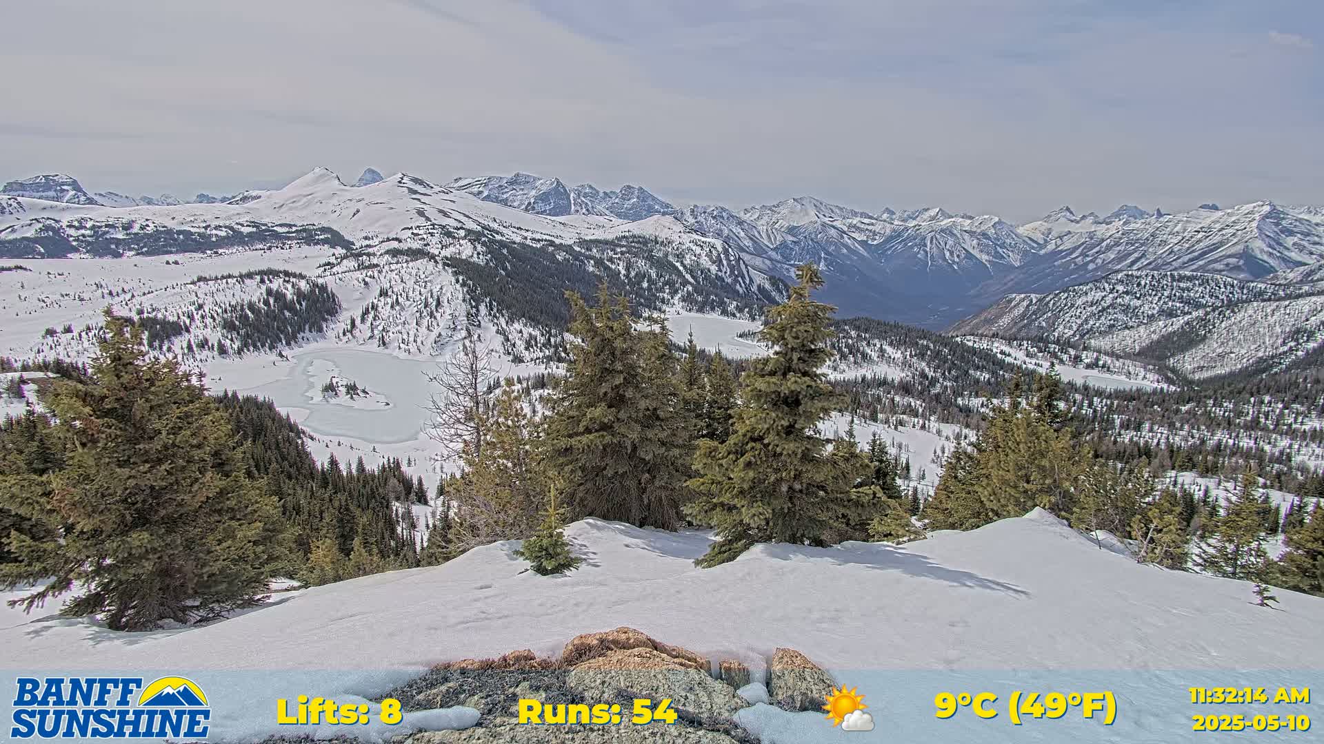 A snow-covered mountain landscape with evergreen trees and a partially frozen lake is visible under partly sunny skies.