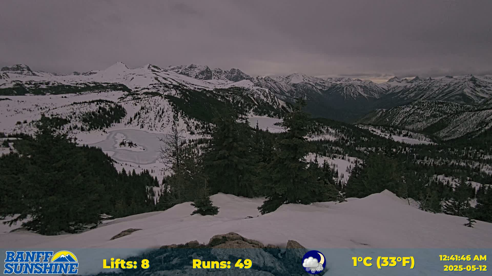 A snow-covered mountain range is visible under an overcast sky, with a partially frozen lake nestled in a valley below.