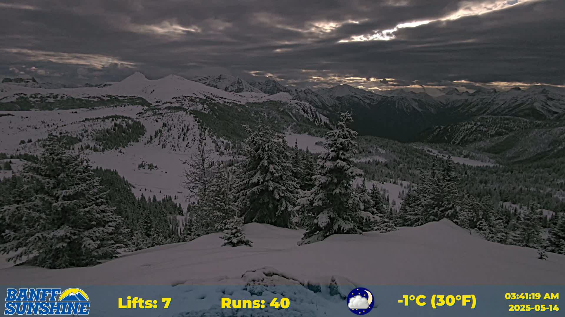 A snow-covered mountain range is visible under a dark, cloudy sky, with some sunlight breaking through the clouds.