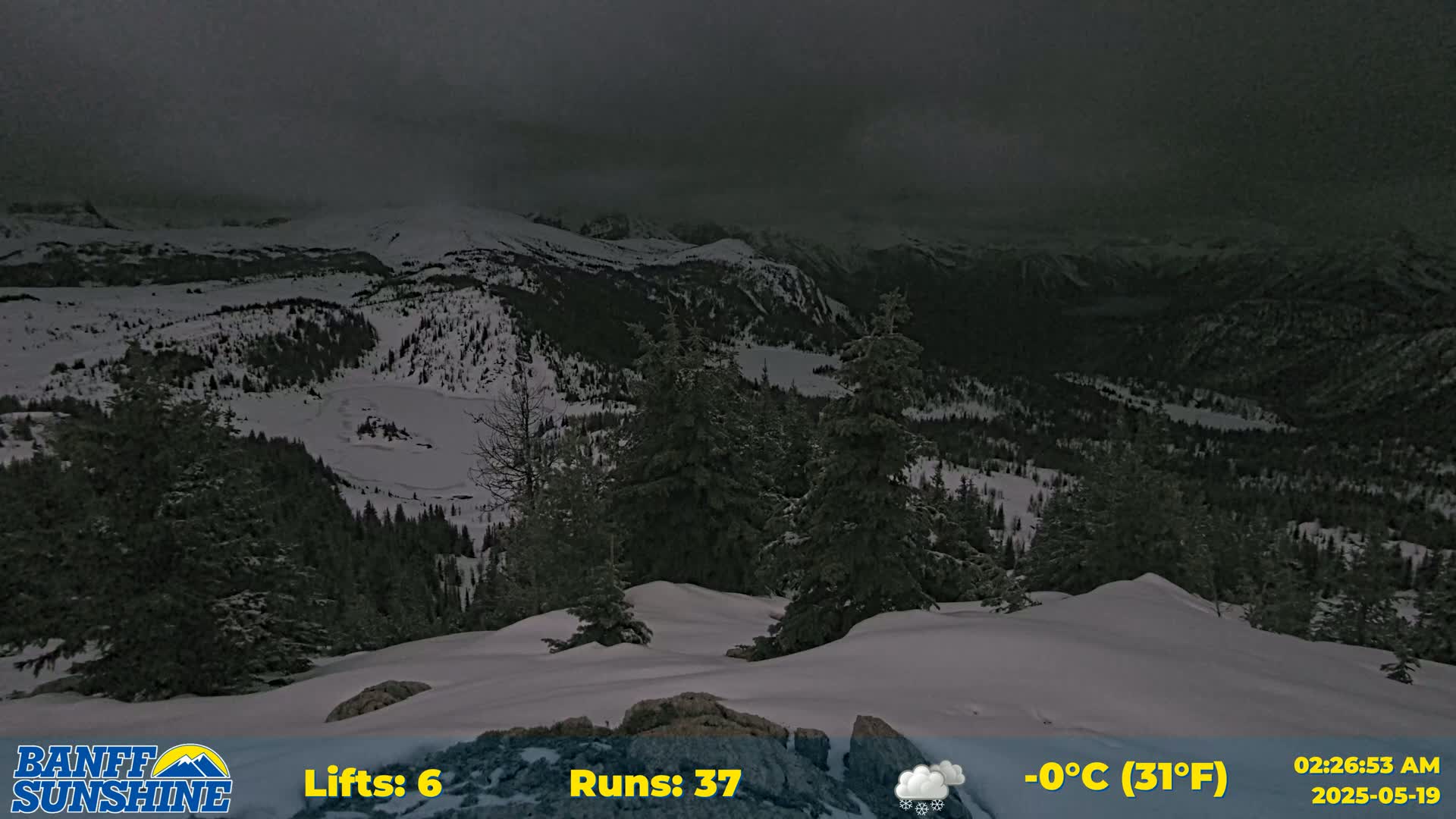 A snow-covered mountain landscape under a dark, cloudy sky, with a few evergreen trees visible in the foreground.