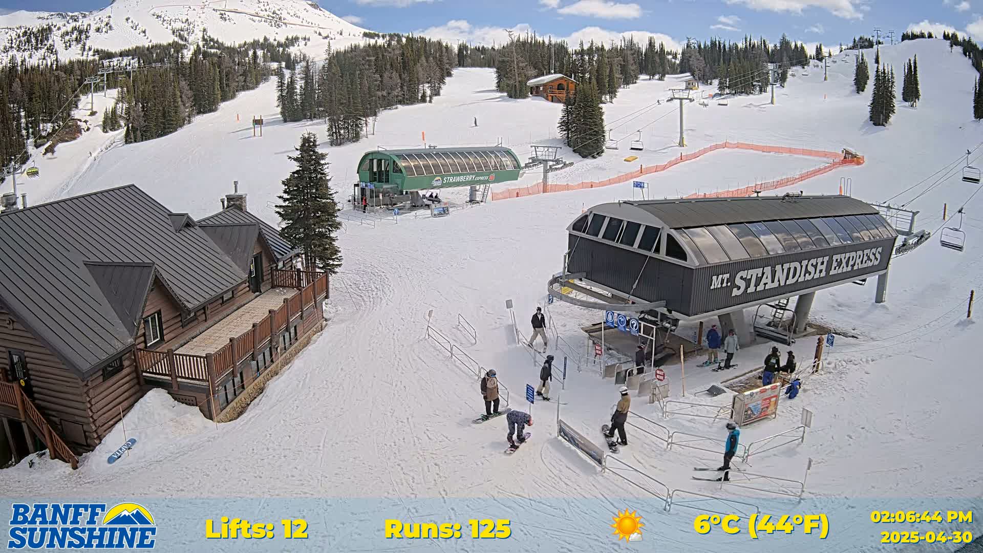 A ski resort on a sunny day shows several chairlifts, a lodge, and skiers and snowboarders on a snow-covered mountain.