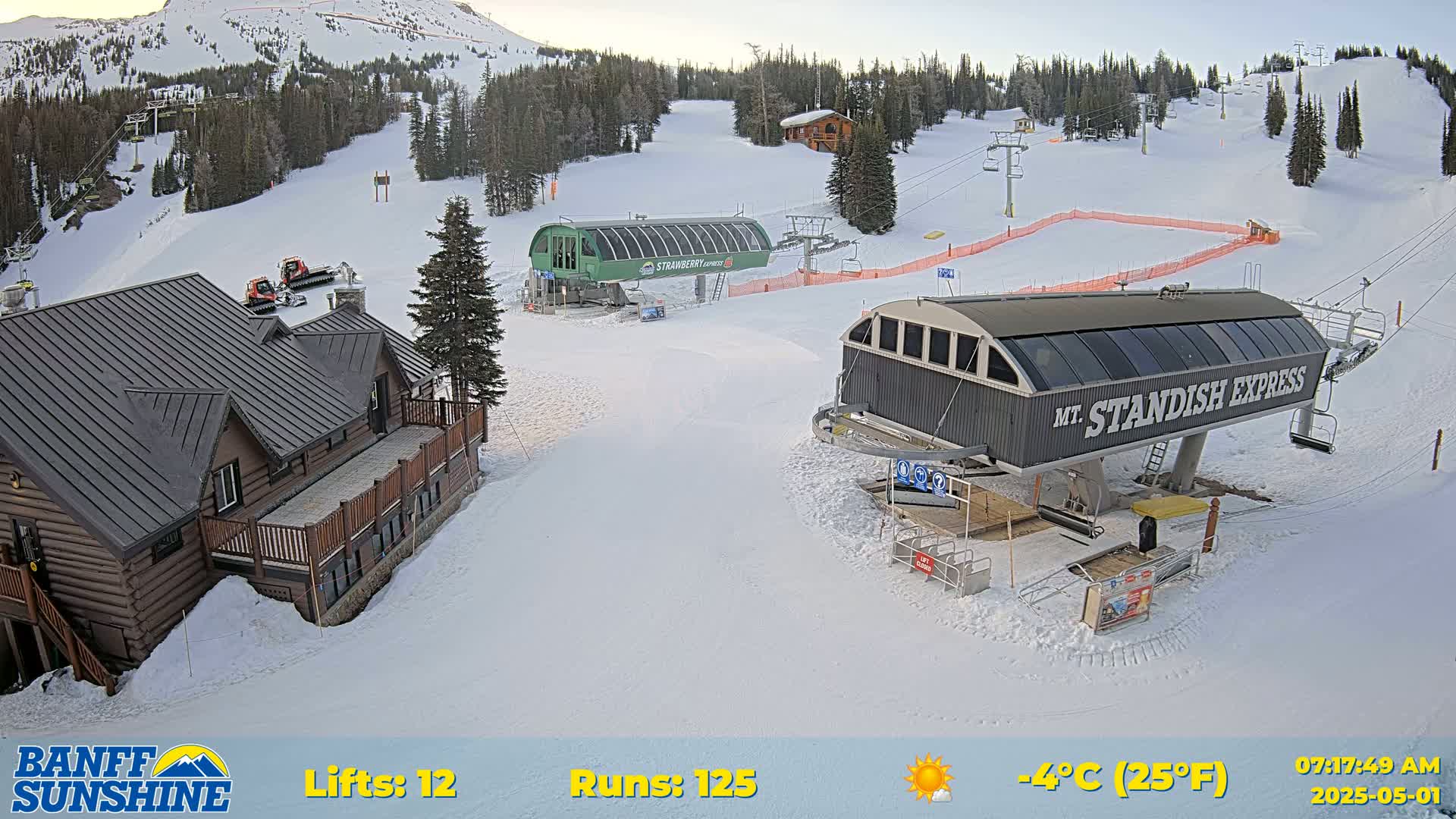 A snow-covered ski resort with two chairlifts, a lodge, and several snowcats visible on a sunny, cold morning.