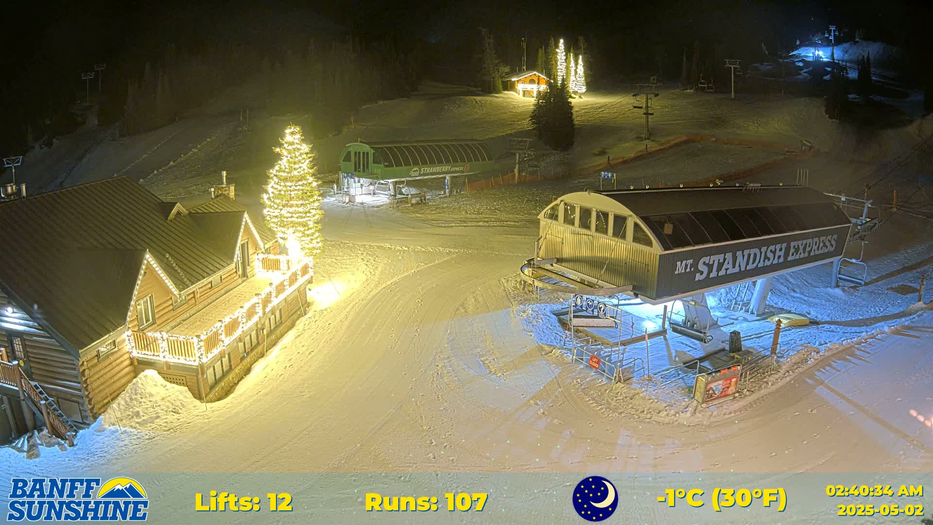 A nighttime view of a snow-covered ski resort with illuminated buildings and ski lifts, under a clear, cold sky.