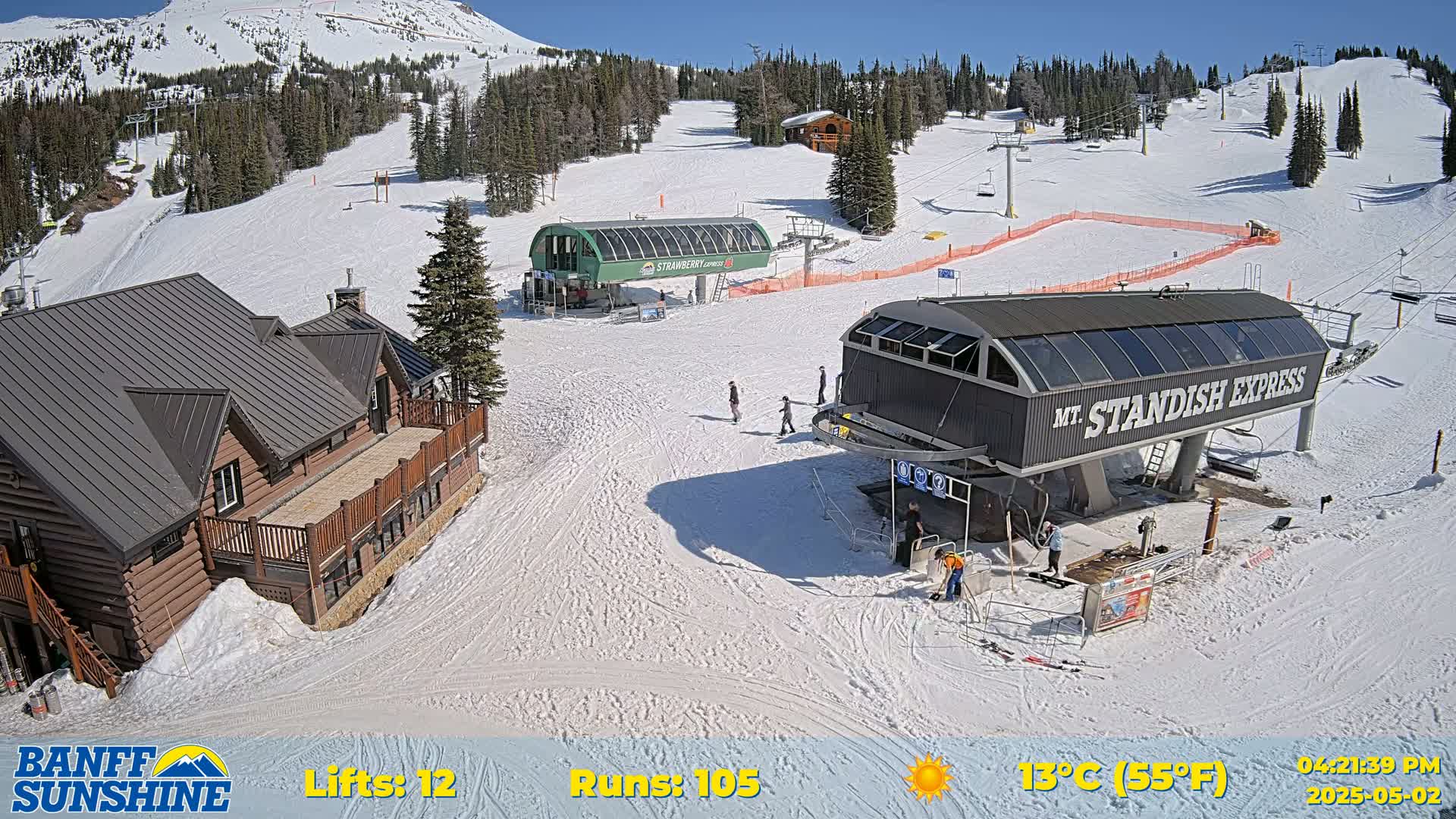 A sunny ski resort scene shows two ski lifts, a log cabin, and several skiers on a snow-covered mountainside.