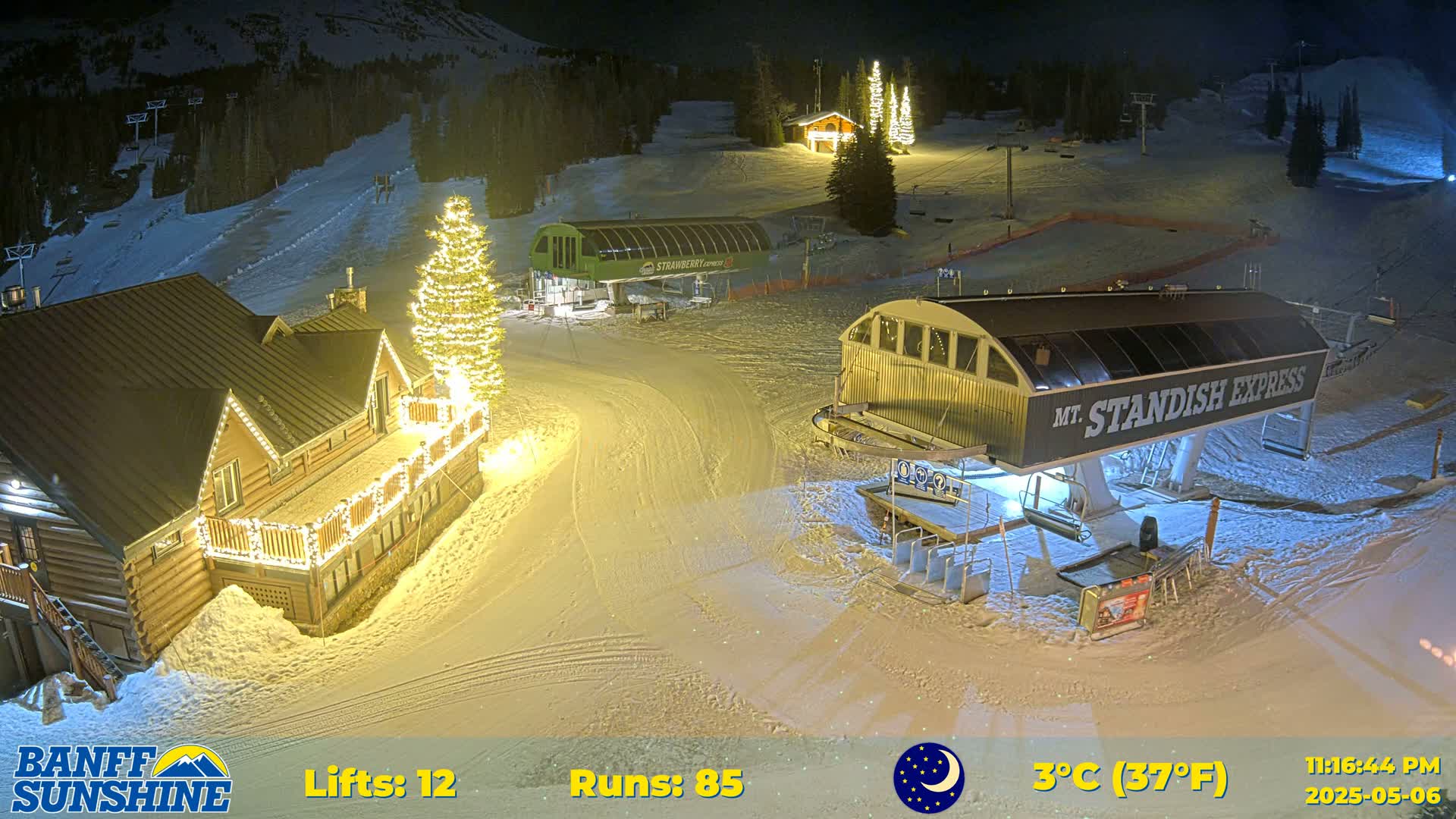 A nighttime view of a snow-covered ski resort with illuminated buildings and ski lifts, under a clear sky.