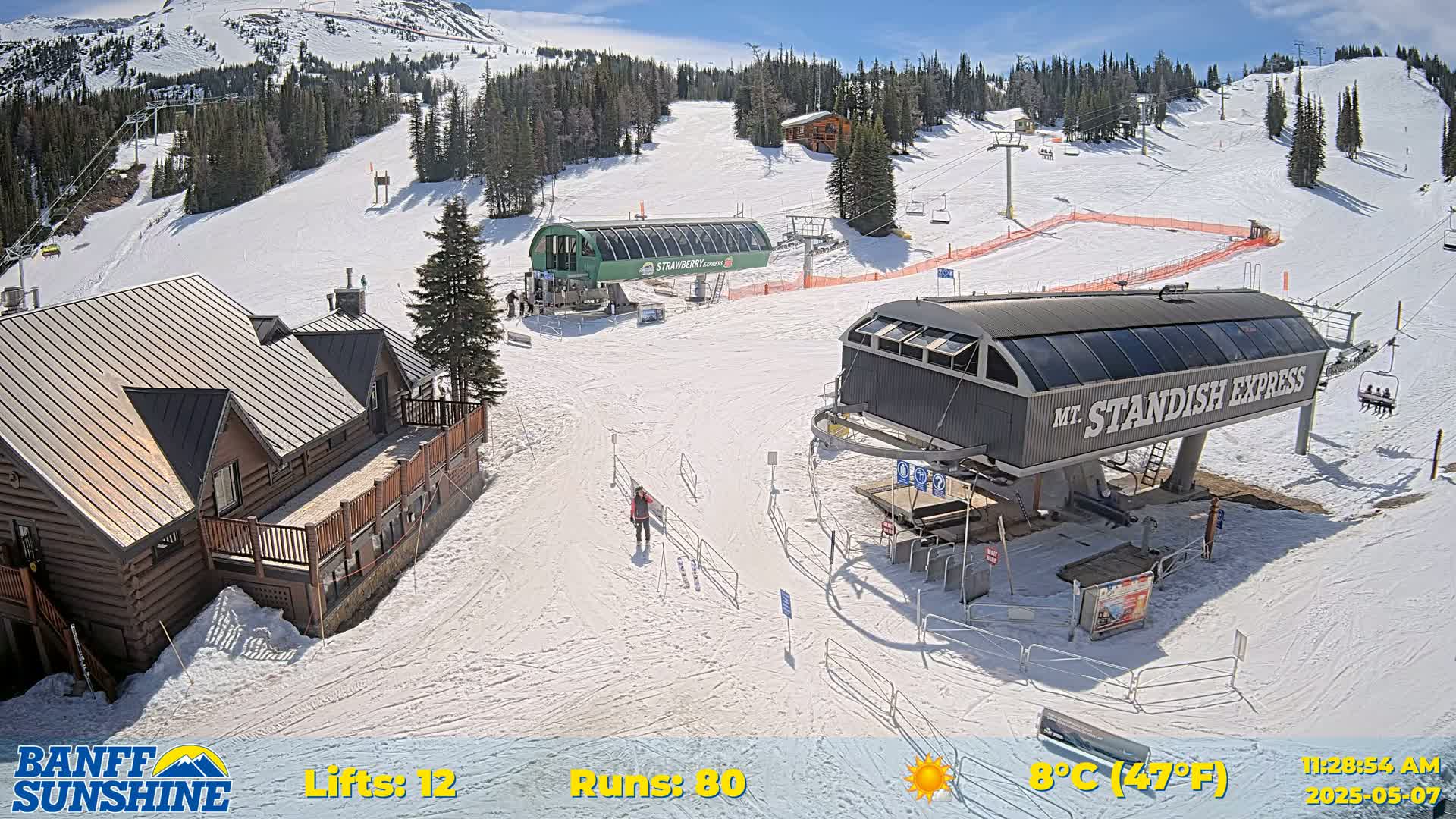 A sunny ski resort scene shows two chairlifts, a log cabin, and skiers on a snow-covered mountain slope.
