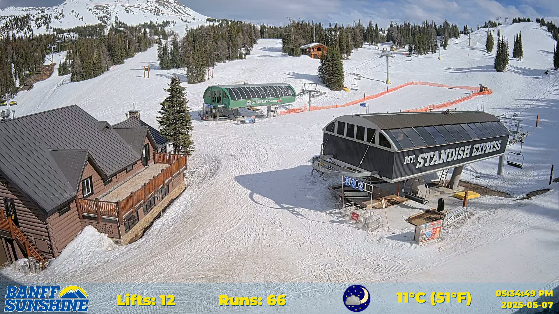 A snow-covered ski resort on a sunny day, showcasing two chairlifts, a log cabin, and several ski runs.