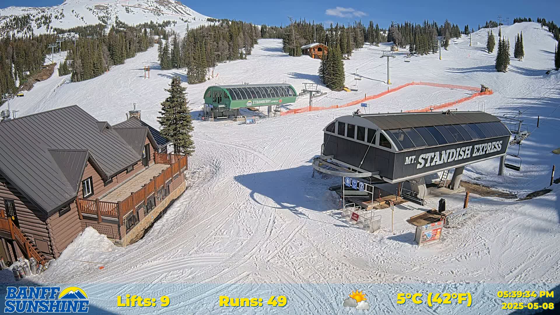 A ski resort on a sunny day with snow-covered slopes, two chairlifts, and a log cabin.