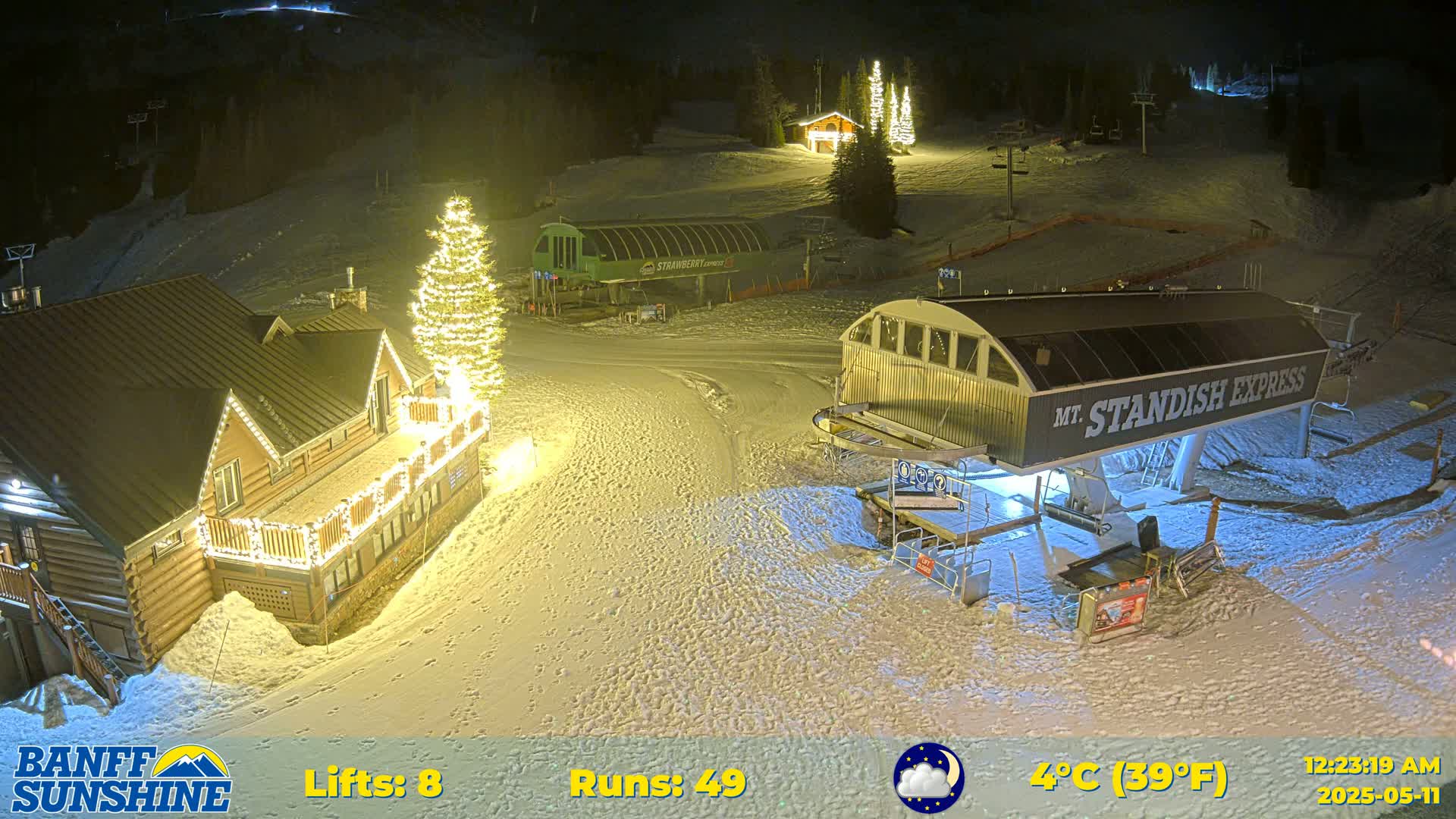 A nighttime snow-covered ski resort scene shows a lit-up lodge, ski lifts, and a Christmas tree, under a clear, cold sky.