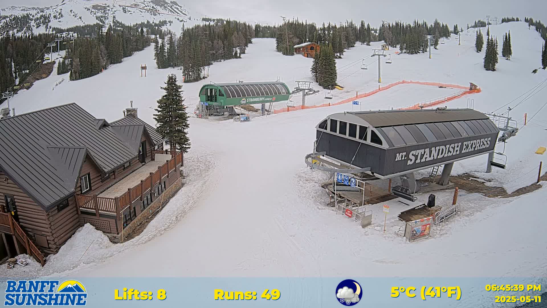 A snow-covered ski resort with two chairlifts, a log cabin, and overcast skies, at 5°C (41°F).